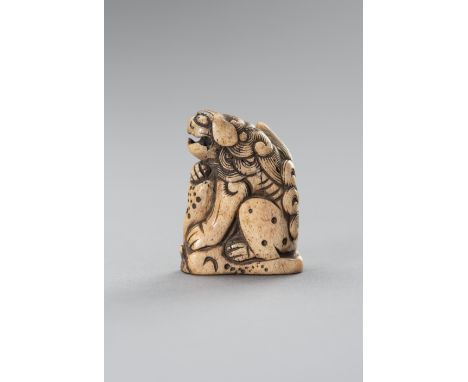 A STAG ANTLER NETSUKE OF A SHISHI ON A ROCKJapan, Edo period (1615-1868)Carved seated, with the front legs placed onto a rock
