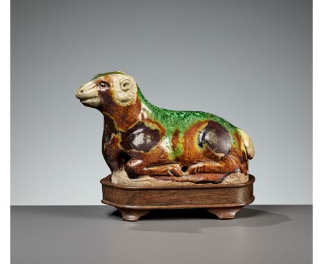 A RARE SANCAI-GLAZED POTTERY FIGURE OF A RAM, TANG DYNASTYChina, 618-907. Well potted as a recumbent ram in an alert position
