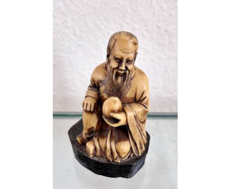 Netsuke, sitzender bärtiger Mann. Bein, auf schwarzem Holzsockel sitzend. Höhe: 5 cm. Skulptur, Japan, wohl 18. Jahrhundert.