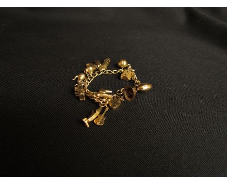 A 9ct gold charm bracelet with padlock clasp, hung with various charms including mirrors lamp, boat, rugby ball etc