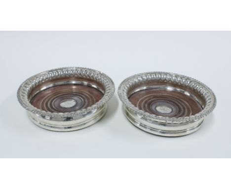 A matched set of two early 19th century silver wine bottle coasters, crested with turned wooden bases and gadrooned rims, one