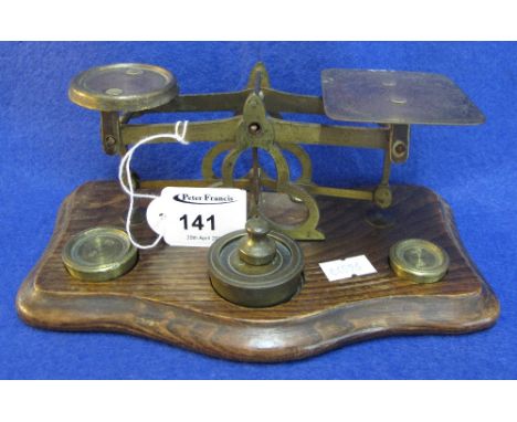 Small set of brass postal scales and weights on serpentine shaped oak base.