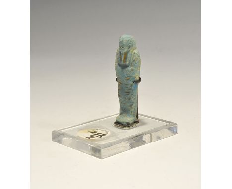 ". A blue glazed composition shabti with tripartite wig and agricultural tools in the crossed hands, panel of hieroglyphic te