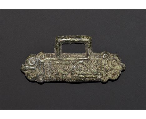 "9th-12th century AD. A flat-section bronze plaque with scrolled trefoil terminals, median panel with scrolls and pellets, re