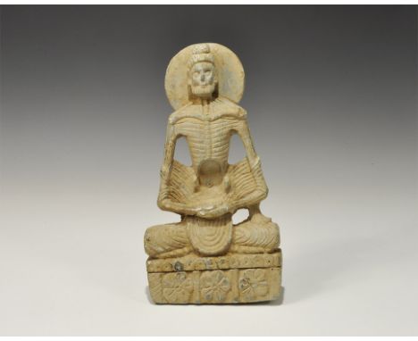 ". An undated archaistic carved schist figure of the Buddha in emaciated form seated cross-legged with hands folded in the la