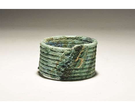 "1200-500 BC. A broad bracelet made from spiral-wound bronze rod; impression of an adjacent textile to the outer face. 201 gr