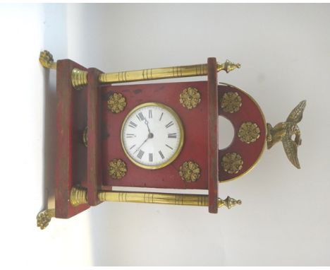 An Empire style mantel clock with eagle surmount over a red painted wooden case, with white enamel dial, flanked by brass pil