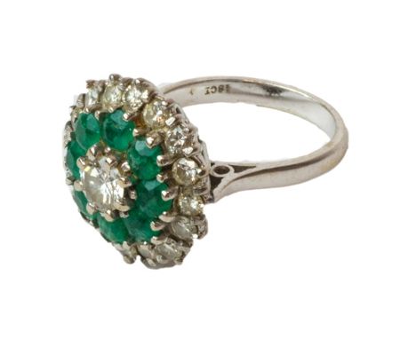 A white gold, diamond and emerald set cluster ring, claw set with the principal circular cut diamond at the centre, within a 