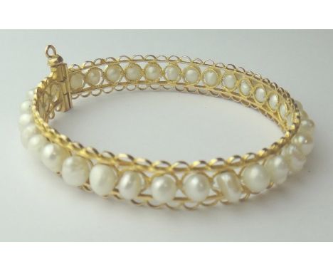 A gold and freshwater cultured pearl bangle, probably Middle Eastern, decorated with pierced borders, gross weight 19 gms.