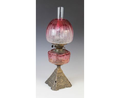 A Victorian brass and cranberry glass oil lamp, 19th century, the cast brass base of pyramidal form with relief moulded panel