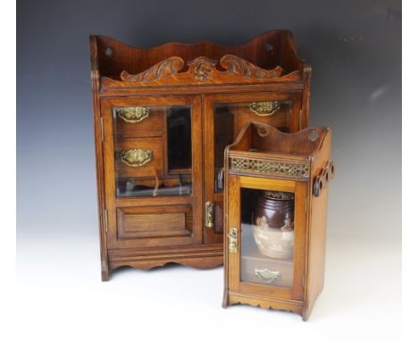 An early 20th century oak smokers cabinet, the carved pediment above a pair of glazed doors opening to a central recess enclo