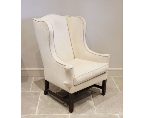 A George III style wing back fireside armchair, early 20th century, in cream fabric applied with rope piping, the curvilinear