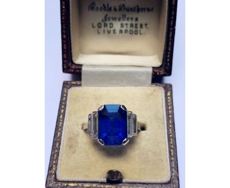 An Art Deco sapphire and diamond ring, the central octagonal step cut sapphire (measuring 11.79mm L x 8.4mm W x 6.1mm D), wit