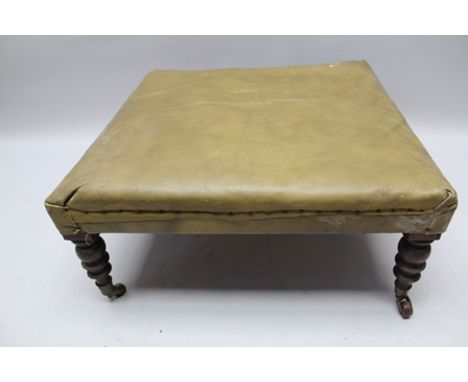 A 19TH CENTURY LOW SQUARE FOOTSTOOL, upholstered in green leather, having ring turned mahogany supports with brass casters, 7