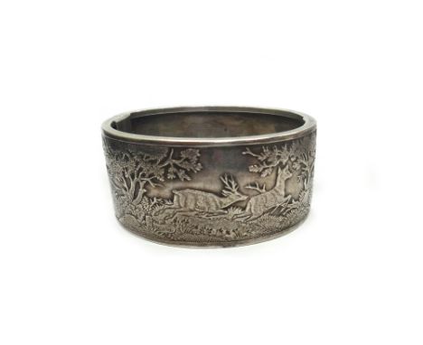 An early 20th century white metal broad hinged bangle, engraved and chased with panels depicting pheasants amidst trees and f