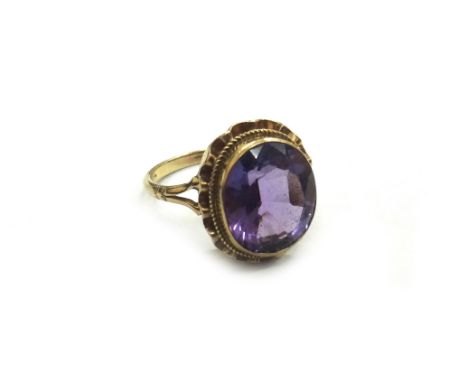 A 9ct gold and amethyst single stone ring, the oval mixed cut stone rub-over set within ropework and undulating borders, hall