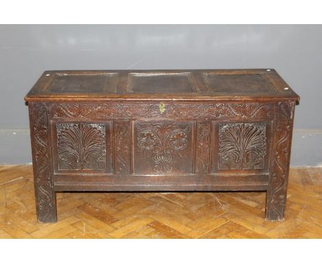 An early 18th century oak coffer, the three panel top over carved frieze and anthemion decorated front, enclosing a candle bo