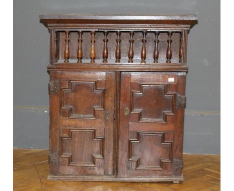 An 18th century and later oak wall cupboard, the plank top over a hinged spindle guarded shelf and a pair of geometrically mo