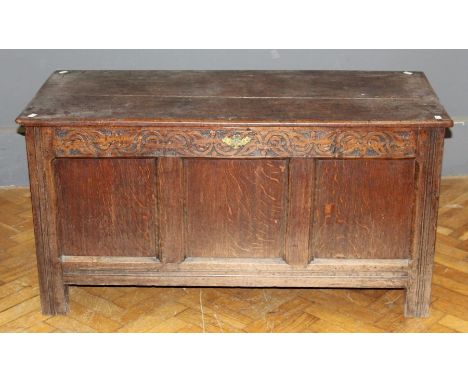 An 18th century oak coffer, the plank top with later hinges, over a scroll carved frieze and three panel front enclosing a va