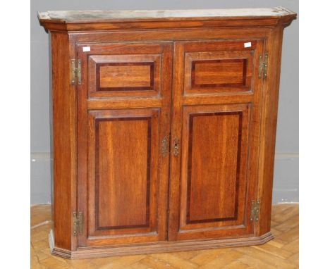 A 19th century oak wall cupboard, the moulded cornice over a pair of mahogany banded fielded panel doors enclosing two shelve