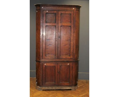 A George III oak floorstanding corner cupboard, the moulded cornice over a pair of panelled doors enclosing three serpentine 