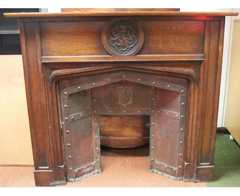 An early 20thC oak fire surround, the plain moulded top, raised above a circular carved lion crest and a shaped opening with 