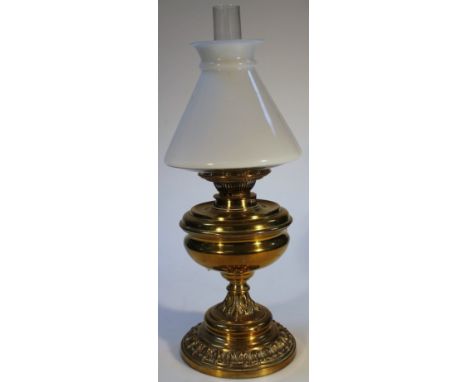 An early 20thC brass oil lamp, with shaped milk glass shade and clear funnel, above a shaped inverted body, with acanthus lea
