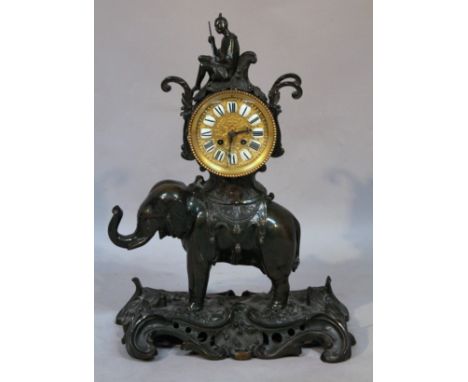 A patinated bronze elephant mantel clock, the circular textured gilt metal dial, with enamel Roman numerals, half striking on