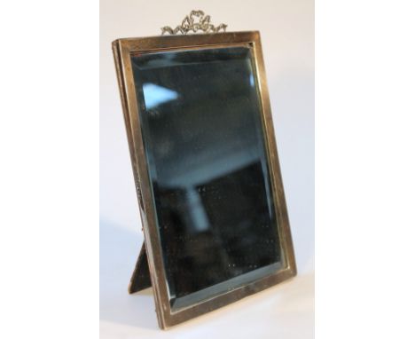 A George V silver framed table mirror, of rectangular form headed by a ribbon and scroll finial with a pressed leather easel 
