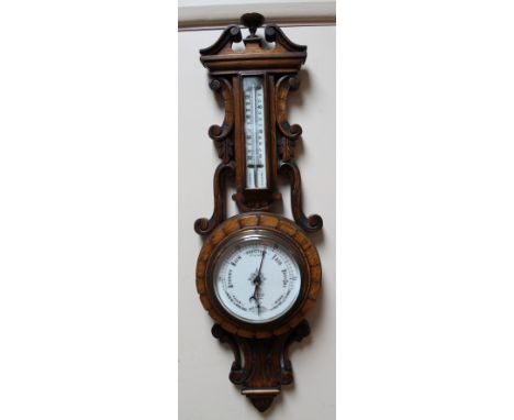 An early 20thC oak cased barometer and thermometer. The circular dial in a heavily carved case. 66cm high.