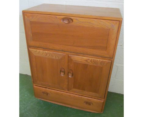 An Ercol Golden Dawn cabinet with drop down front above two cupboard doors and drawer