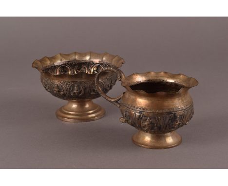 A vintage Indian white metal sugar basin and milk jug, with wavy rims above panels of deities, approx 5.8ozt. (2) 