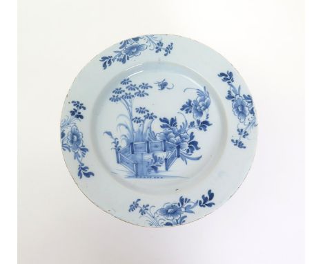 A Liverpool delftware charger  mid 18th century, painted in blue with bamboo and peony issuing from an ornamental fence, an i
