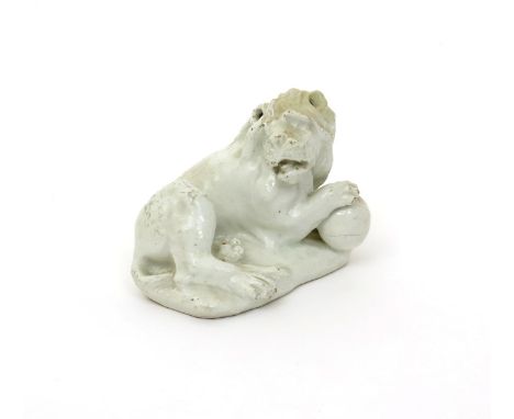 A Bow white-glazed model of a lion  c.1753, recumbent with head turned to dexter and resting his right forepaw on top of a ba