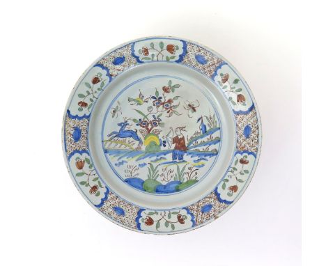 A large delftware charger  c.1740, painted in blue, red, green and yellow with a Chinaman hunting a stag with a bow and arrow