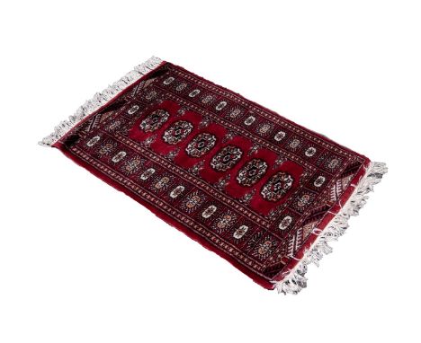 PAKISTAN BOKHARA RUG with an intricate design of three rows of primary guls on a wine field, broad centric border with end pa