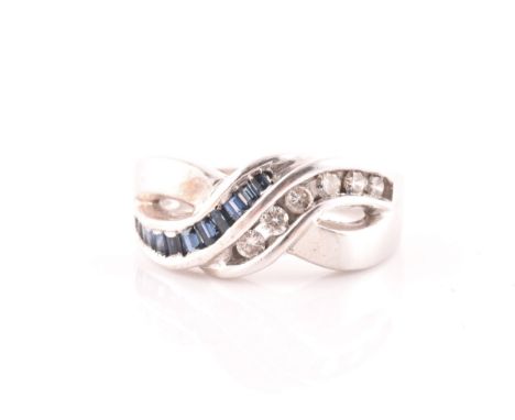 A 14ct white gold, diamond, and sapphire crossover ring, channel-set with mixed calibre-cut sapphires and round brilliant-cut