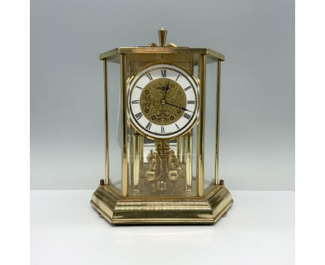 This vintage clock features a brass frame and finish, and displays an analog clock face. The clock has quartz movement and re