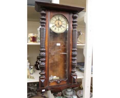 A German wall clock, mahogany frame with turned pilasters, pediment to top and bottom with cream enamel dial, Roman numerals;