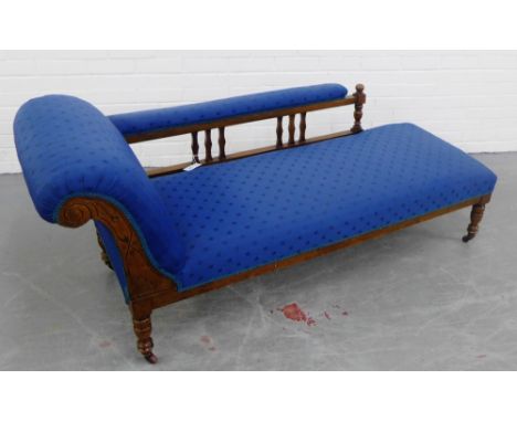 A late 19th / early 20th century carved walnut framed chaise-longue with spindle and padded back, upholstered in blue fabric,