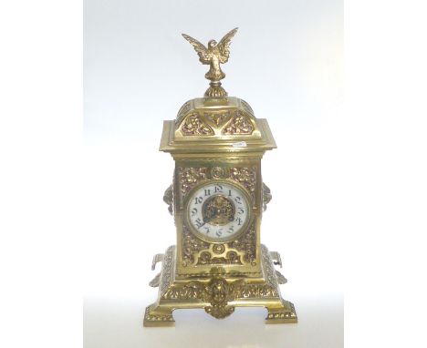 Ornate brass mantel clock with pierce work top and sides, cherub and lions masks, enamel dial, topped with open winged bird