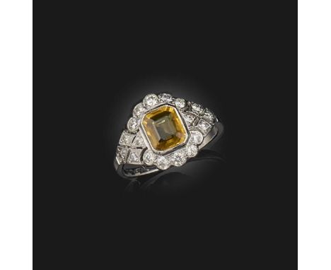 A yellow sapphire and diamond ring, set with a step-cut yellow sapphire within diamond cluster surround, the sapphire weighin