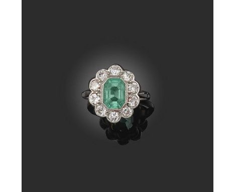 An emerald and diamond cluster ring, the step-cut emerald set within a surround of circular-cut diamonds in white gold and pl