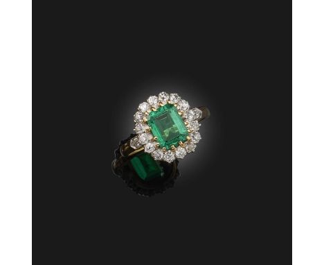 An emerald and diamond ring, France, early 20th century, of cluster design, set with a step-cut emerald weighing 1.29 carats,