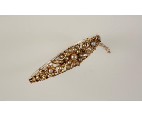 A VICTORIAN PEARL BANGLE, the hinged top open section set overall with graduated pearls, forming a triple flowerhead and leaf