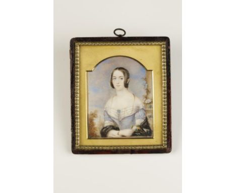 A PAINTED PORTRAIT MINIATURE OF A SEATED LADY, wearing a blue dress and jewellery, with a landscape behind, in a leather fram