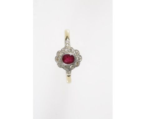 A RUBY AND DIAMOND CLUSTER RING, the central oval-cut ruby collet-set and surrounded by a rub-over millegrain set border of t