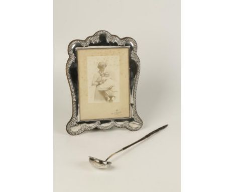 AN EDWARDIAN PHOTOGRAPH FRAME of shaped rectangular form with a gadrooned border interspersed with embossed flowers, wooden b