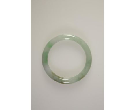 A CHINESE JADE BANGLE of plain circular form, the celadon colour with dark to light green tones throughout, 9cms dia. See ill