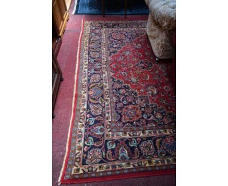 A BURGUNDY GROUND MASHAD CARPET, with central floral medallion and all-over floral pattern, inside a wide conforming border w